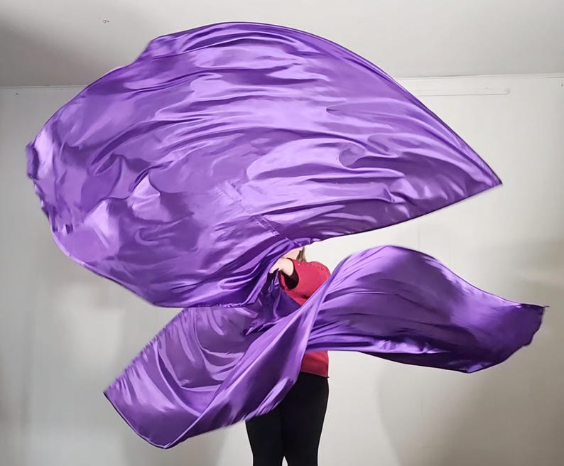 May include: A purple satin dance flag, flowing in the air. The flag is held by a person wearing a red shirt and black pants.