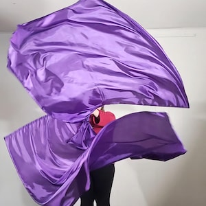 May include: A person is holding two purple dance flags, which are flowing in the air. The flags are made of a silky fabric and are a vibrant purple color.