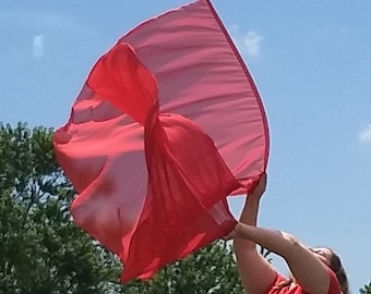 Op de afbeelding: Een persoon houdt een rode stoffen vlag in de lucht. De vlag wappert in de wind en de persoon draagt een rood shirt.