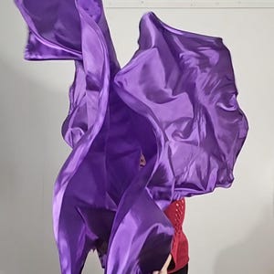 May include: A person is holding and twirling two purple fabric dance flags. The flags are flowing in the air.