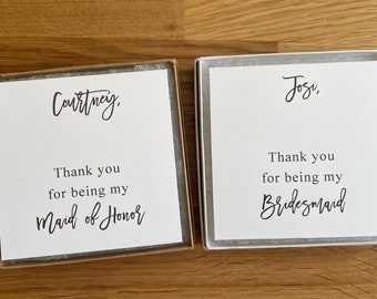 May include: Two white cards with black text. The top card says "Courtney, Thank you for being my Maid of Honor". The bottom card says "Josi, Thank you for being my Bridesmaid".
