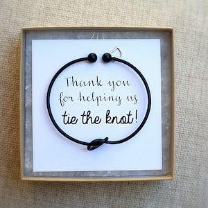 May include: A black bracelet with a knot design, presented in a small box. The bracelet is on a white card with the text "Thank you for helping us tie the knot!" in a handwritten style font.