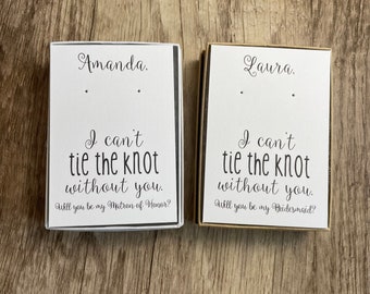 May include: Two white boxes with black text. The top box says "Amanda. I can't tie the knot without you. Will you be my Matron of Honour?" The bottom box says "Laura. I can't tie the knot without you. Will you be my Bridesmaid?"