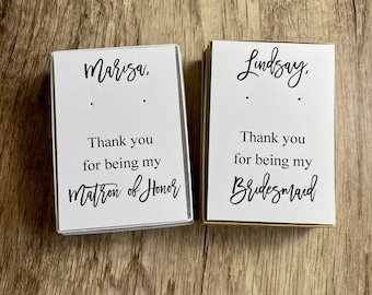 May include: Two white boxes with black text. The top box says "Marisa, Thank you for being my Matron of Honor". The bottom box says "Lindsay, Thank you for being my Bridesmaid".