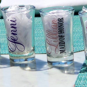 May include: Four clear glass shot glasses with personalized names and titles, including "Anabel", "Jenni", "Lillian Maid of Honor", and "Nicole".