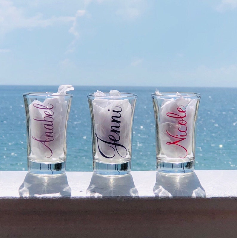 May include: Three clear glass shot glasses with the names "Annabel", "Jenni", and "Nicole" written on them in different colors.