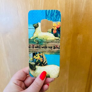 May include: A phone case with a blue background and a white sheep with the text "It is well with my soul" on it.