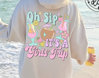 Może przedstawiać: Beżowa bluza z kapturem z grafiką na plecach z napisem "Oh Sip It's A Girls Trip" z ilustracjami koktajli. Bluza z kapturem ma również tekst "Hygge Day" w okręgu. Osoba stoi na plaży.