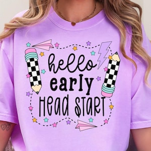 May include: A light purple t-shirt with the words "hello early head start" in black script. The design includes two pencils with checkered patterns, stars, paper airplanes, and a lightning bolt.