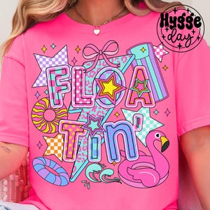 May include: Pink t-shirt with a graphic design featuring the text "Floatin'" in a colorful, retro style. The design includes stars, a flamingo, a pool float, and a checkered pattern.