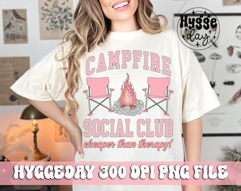 May include: A white t-shirt with a pink graphic design that says "Campfire Social Club cheaper than therapy!" The graphic includes two pink camping chairs and a campfire with flames.