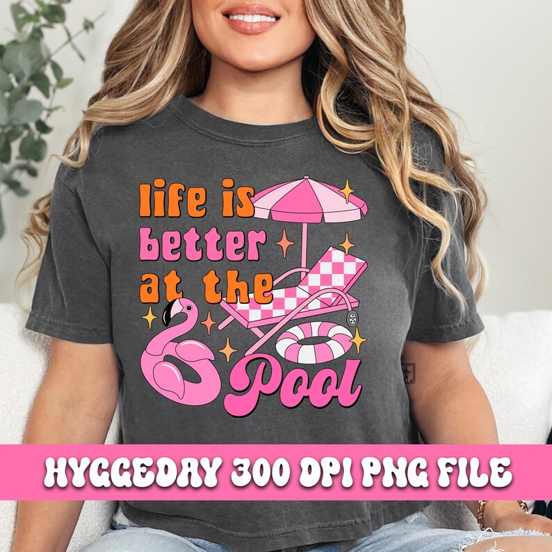 Pode incluir: Uma camiseta cinza com o texto "Life is better at the pool" em letras rosa e laranja. O design tamb&eacute;m inclui um flamingo rosa, uma espregui&ccedil;adeira xadrez rosa e branca, um flutuador de piscina rosa e branco e estrelas.