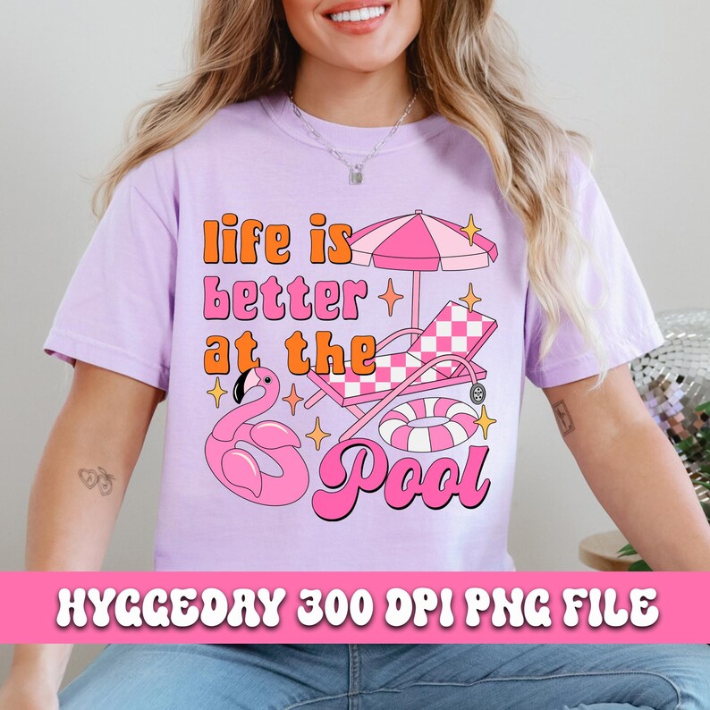 Pode incluir: Uma camiseta rosa com o texto "life is better at the pool" em uma fonte retr&ocirc;. O design inclui um flamingo rosa, uma espregui&ccedil;adeira xadrez, um guarda-sol rosa e branco e um flutuador.