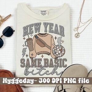 May include: Cream-colored t-shirt with a graphic design featuring the text "NEW YEAR SAME BASIC bitch". The design includes a sweater, fanny pack, disco ball, and lightning bolts in neutral tones. A fun, casual tee.