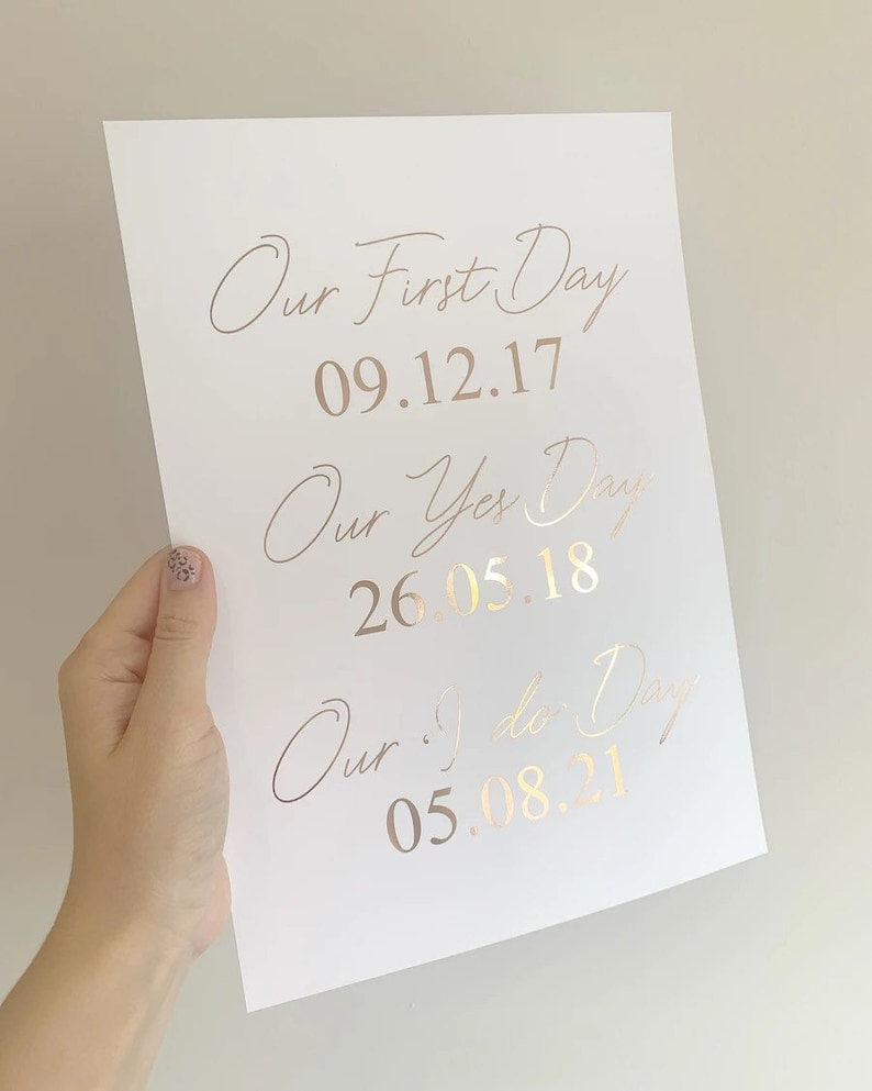 May include: A white card with gold foil lettering that reads "Our First Day 09.12.17", "Our Yes Day 26.05.18", and "Our I Do Day 05.08.21".