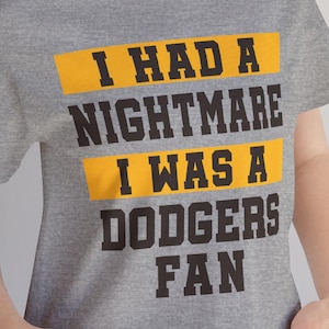 May include: A gray t-shirt with the text "I had a nightmare I was a Dodgers fan" printed on it. The text is in black with a yellow background.