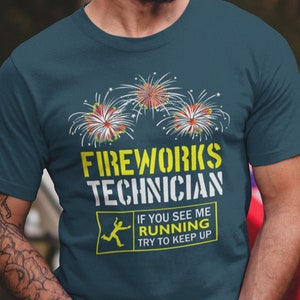 Pode incluir: Uma camiseta azul turquesa com um gráfico amarelo de fogos de artifício e o texto "Fireworks Technician". O gráfico também inclui uma placa amarela com uma figura de palito correndo e o texto "Se você me vir correndo, tente acompanhar".