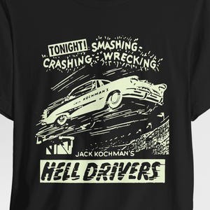 Puede incluir: Camiseta negra con un gráfico retro de un coche en el aire, acompañada del texto "TONIGHT! SMASHING, CRASHING, WRECKING" y "JACK KOCHMAN'S HELL DRIVERS" en una fuente vintage.