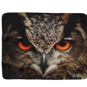 May include: Close-up of an owl's face with bright orange eyes. The owl's feathers are brown and black.