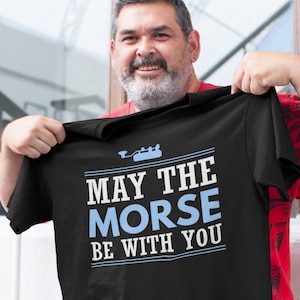 May include: Black t-shirt with a white graphic that says "May the Morse be with you". The graphic also includes a blue illustration of a Morse code machine.