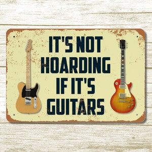 May include: A yellow and brown metal sign with the text "It's not hoarding if it's guitars" and two images of guitars on either side of the text.