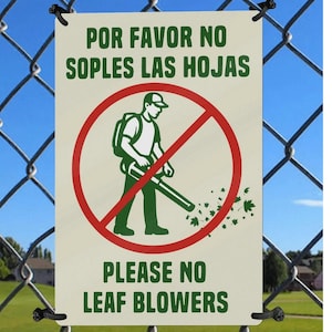May include: A rectangular sign with the text "POR FAVOR NO SOPLES LAS HOJAS" and "PLEASE NO LEAF BLOWERS". The sign features a red circle with a crossed-out image of a person using a leaf blower. The sign is attached to a chain-link fence.