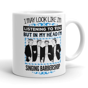 May include: White ceramic mug with a blue and black design. The mug features a graphic of four men in suits and hats singing. The text on the mug reads "I may look like I'm listening to you but in my head I'm singing barbershop."
