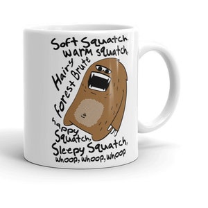 May include: White ceramic mug with a brown cartoon creature with a band-aid on its chest. The creature is surrounded by text that reads "Soft Squatch, warm squatch, Hairy forest Brute, happy Squatch, Sleepy Squatch, whoop, whoop, whoop".
