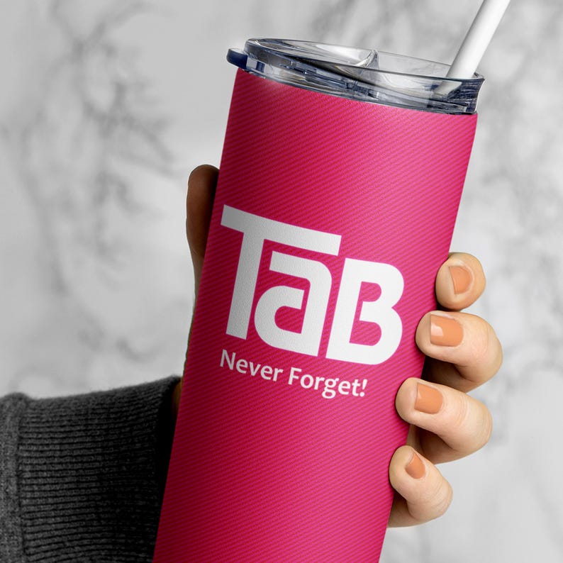 May include: A pink stainless steel tumbler with a white "Tab Never Forget!" logo. The tumbler has a black lid and a straw.