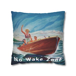 May include: A vintage-style throw pillow with a blue background featuring a family of three on a wooden boat with the text "No Wake Zone" in white letters.