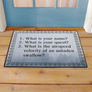 May include: A black doormat with a white background and a decorative border. The text on the doormat reads: "1. What is your name? 2. What is your quest? 3. What is the airspeed velocity of an unladen swallow?"