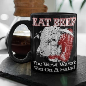 May include: Black coffee mug with a white bull illustration and the text "Eat Beef The West Wasn't Won On A Salad".