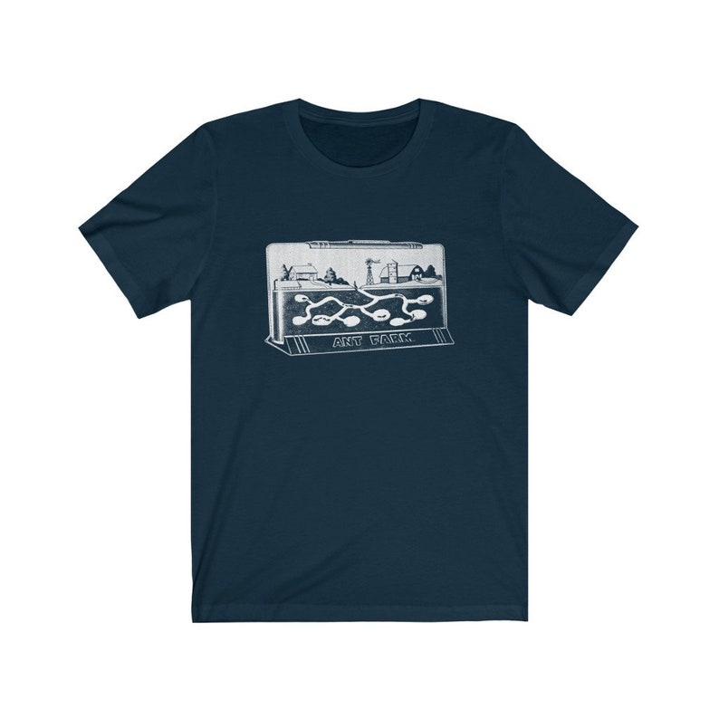 May include: A navy blue t-shirt with a white graphic of an ant farm. The graphic shows a small plastic ant farm with a miniature town inside and ants crawling through tunnels. The text "ANT FARM" is printed below the graphic.