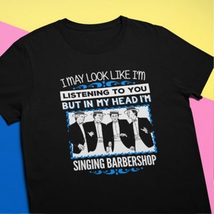 Puede incluir: Camiseta negra con un gráfico blanco de cuatro hombres con traje cantando. El texto dice "Puedo parecer que te estoy escuchando, pero en mi cabeza estoy cantando barbershop."