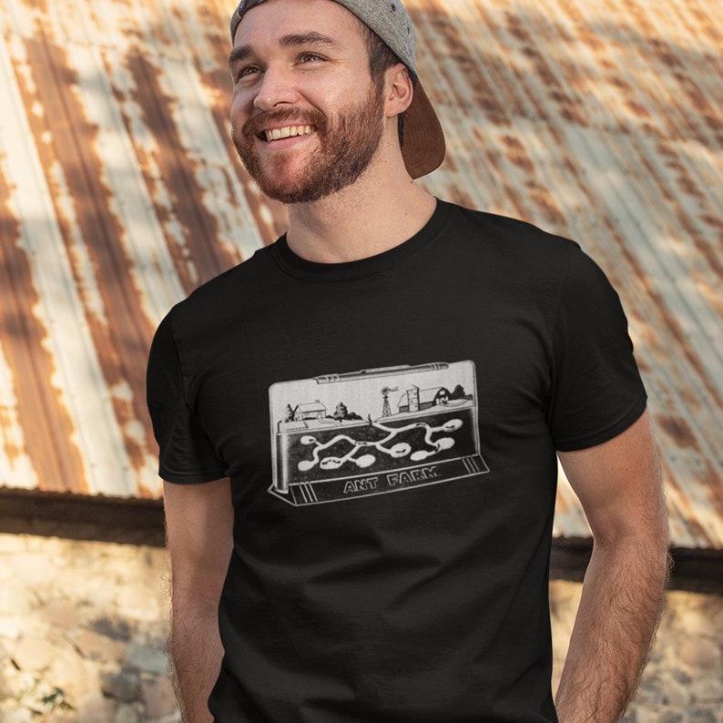 May include: A black t-shirt with a vintage-style illustration of an ant farm. The illustration shows a small ant farm with a path for the ants to travel. The text "ANT FARM" is printed below the illustration.