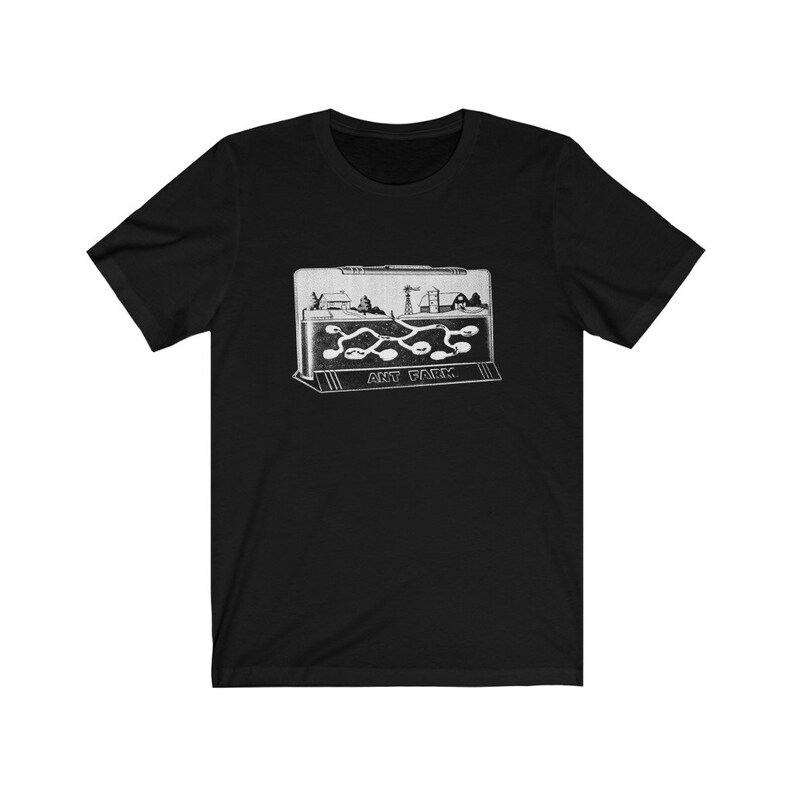 May include: A black t-shirt with a white graphic of an ant farm. The graphic shows a small town with a road and a winding ant trail. The text "ANT FARM" is printed below the graphic.