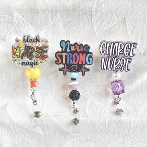 Puede incluir: Tres carretes de insignia con temática de enfermería con diferentes diseños. Uno dice "black nurse magic", otro "Nurse Strong" y el tercero "Charge Nurse". Cada carrete tiene un diseño único de cuentas y dijes.