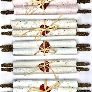 May include: Five rolled up scrolls with decorative brass ends and tied with twine and a red wax seal. The scrolls are made of white paper with flecks of color.
