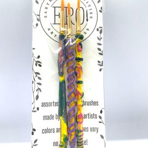 May include: Three paintbrushes with colorful, textured handles. The handles are yellow, purple, and green with swirls and dots. The brushes are packaged on a white card with the text "EARTH RARE ODDITIES ERO ART" and "assorted brushes made by artists colors and sizes vary no two alike!"