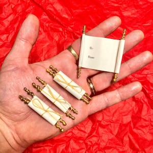 May include: Four miniature scrolls with gold accents and a white background. The scrolls are tied with twine and have the words "To:" and "From:" written on them.