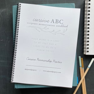 May include: A white, spiral-bound workbook with the title "cursive ABC scripture memorization workbook". The cover features a gray branch with leaves and the text "Your word is a lamp to my feet and a light to my path - Psalm 119:105". The bottom of the cover reads "Cursive Penmanship Practice" and includes the social media handle "@pipandjpapery" and website "www.pipandjpapery.com".
