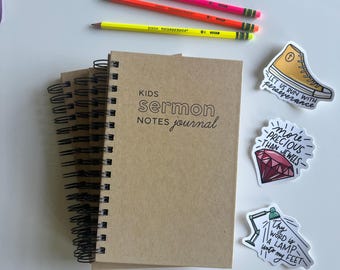 Op de afbeelding: Drie bruine spiraalgebonden notitieboekjes met de tekst "KIDS sermon NOTES journal" op de voorkant. De notitieboekjes zijn omringd door kleurpotloden en stickers met religieuze citaten.