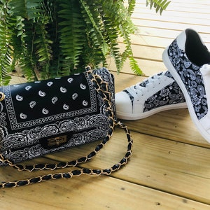 Pu&ograve; includere: Una borsa a tracolla nera e bianca con stampa bandana, con una tracolla a catena dorata e un paio di scarpe da ginnastica bianche con stampa bandana nera e bianca.