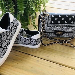 Pu&ograve; includere: Un paio di scarpe da ginnastica bianche con stampa paisley bianco e nero e una borsa a tracolla con catena nera con stampa paisley bianco e nero.