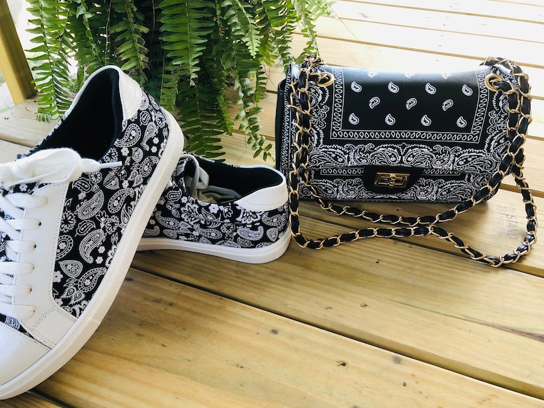 Pu&ograve; includere: Un paio di scarpe da ginnastica bianche con stampa paisley bianco e nero e una borsa a tracolla con catena nera con stampa paisley bianco e nero.