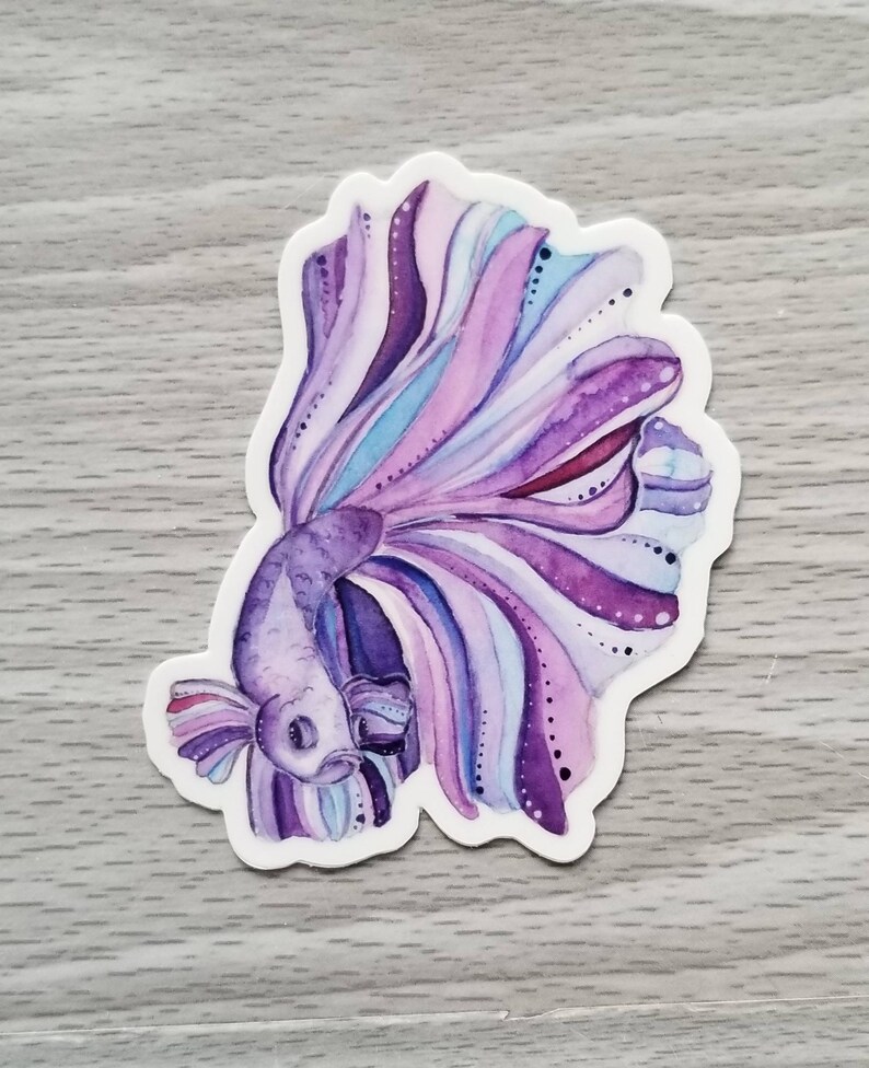 Peut inclure: Un autocollant en aquarelle violet et bleu d'un poisson combattant avec une longue queue flottante.