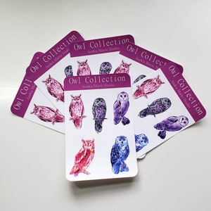 May include: A set of eight colorful owl stickers with the text "Owl Collection" and "Andra Marie Studio" on each sticker. The owls are painted in shades of pink, purple, and blue.