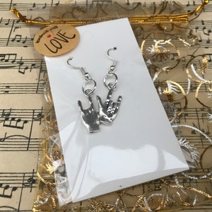 May include: Silver earrings with a rock and roll hand gesture design. The earrings are packaged on a white card with a small tag that says "handmade with love".