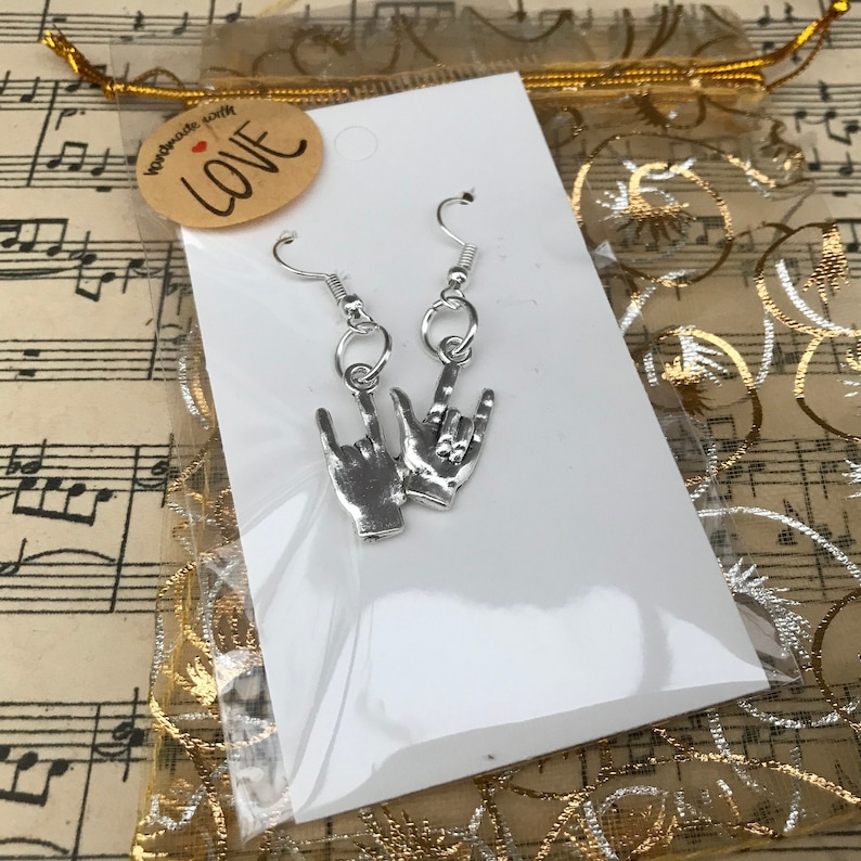 May include: Silver earrings with a rock and roll hand gesture design. The earrings are packaged on a white card with a small tag that says "handmade with love".