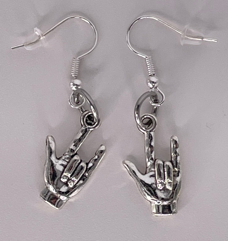 May include: Silver earrings with a hand sign for 'I love you' in American Sign Language.